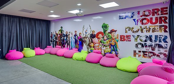 Sala de aula com puffs e chão de grama sintética, em sua parede tem personagens da Disney, Marvel e Pixar.