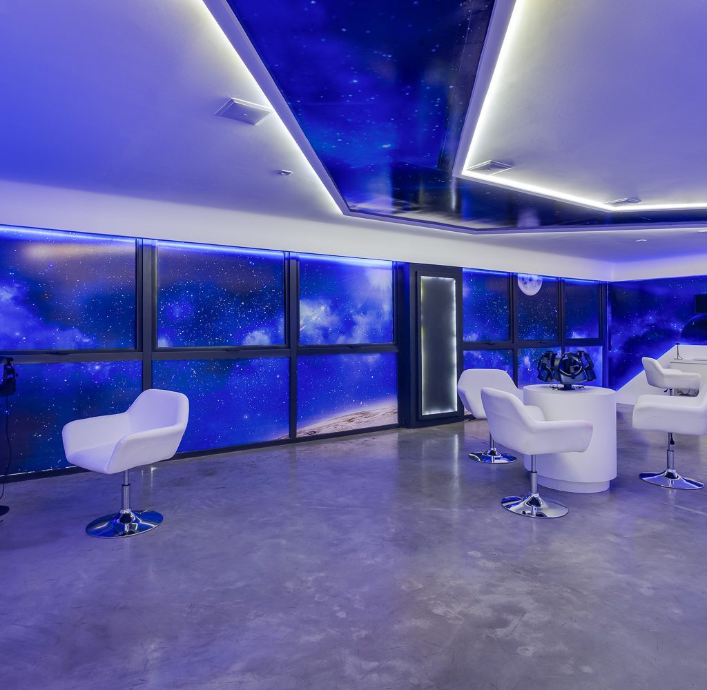 Sala com poltronas brancas, luzes azuis e óculos de realidade virtual.