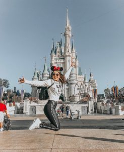 Mulher pulando em frente a um castelo na Disney.