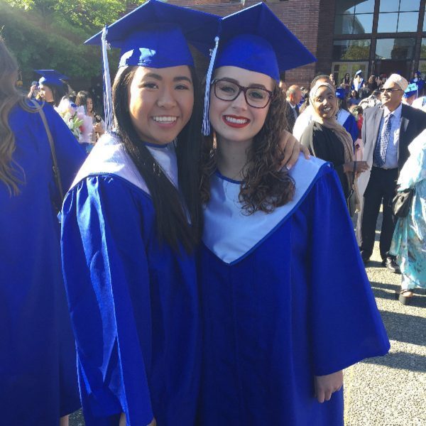 Duas alunas formadas com beca e capelo azul, elas estão sorrindo